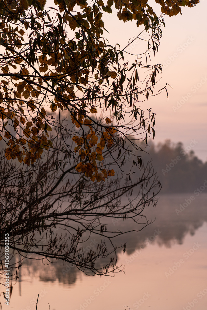 Early morning tranquility at a serene lake with autumn foliage and a distant smokestack reflecting in the calm water Early morning tranquility at a serene lake with autumn foliage and a distant smokestack reflecting in the calm water