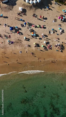 Overhead view of a beach with families and people enjoying the summer. Vertical drone video with lateral displacement. Silhouettes of people's shadows.