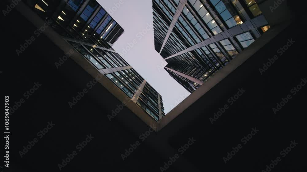 Wide angle gimbal dolly shot downtown high-rise glass skyscrapers in evening, financial district looking up tall modern architecture office buildings city center street, warm lighted windows