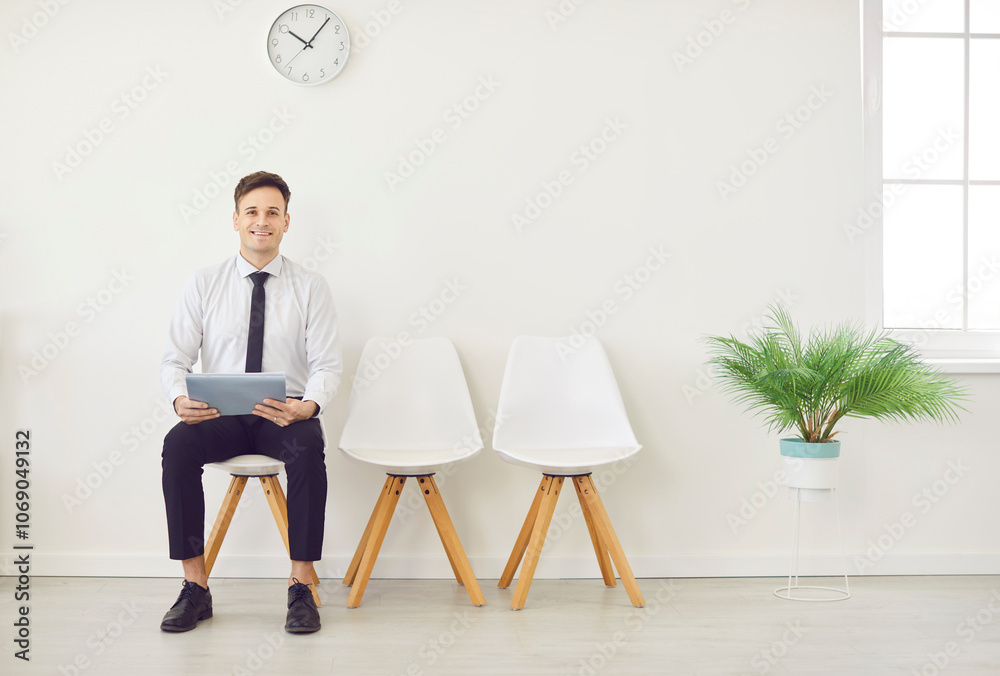 Man job seeker sitting in office with empty chairs waiting for interview invitation turn and looking at camera. Company employee preparing for meeting or conference. Recruitment and business concept. Man job seeker sitting in office with empty chairs waiting for interview invitation turn and looking at camera. Company employee preparing for meeting or conference. Recruitment and business concept.