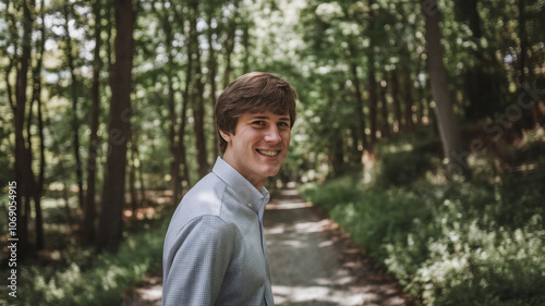 Young Caucasian male smiling on a forest path, showcasing a cheerful vibe amidst lush greenery in a serene outdoor setting.