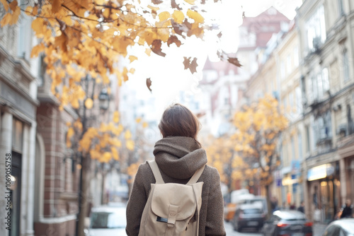 A person walks through picturesque street lined with autumn trees, showcasing vibrant yellow leaves. cozy atmosphere evokes sense of tranquility and reflection photo