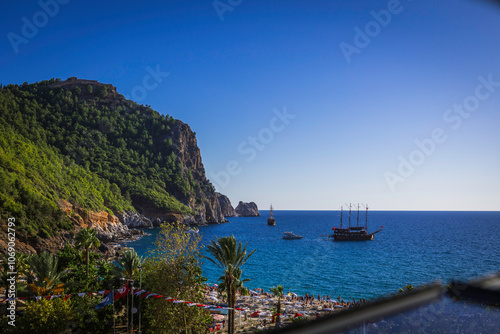 Fototapeta Naklejka Na Ścianę i Meble -  Alanya castle top view on the mountain with coast ferry boat on blue sea . Beautiful cleopatra beach Alanya Turkey landscape travel landmark.