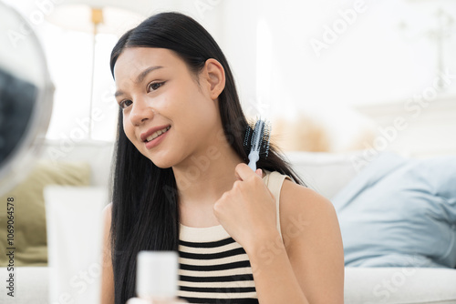 Cheerful young Asian pretty woman combing her beautiful hair with brush while sitting near mirror, looking at mirror with happy and smiling in living room Free Download Cheerful young Asian pretty woman combing her beautiful hair with brush while sitting near mirror, looking at mirror with happy and smiling in living room - GFXLoad