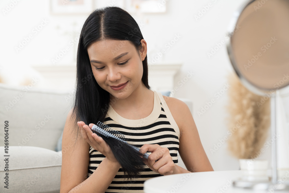 Cheerful young Asian pretty woman combing her beautiful hair with brush while sitting near mirror, looking at mirror with happy and smiling in living room Cheerful young Asian pretty woman combing her beautiful hair with brush while sitting near mirror, looking at mirror with happy and smiling in living room
