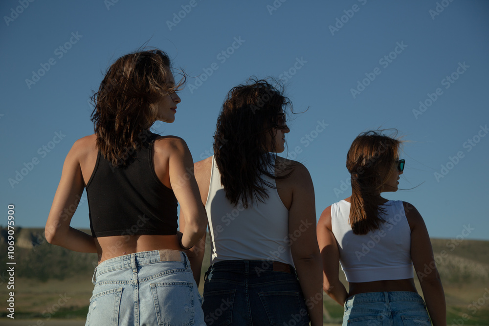 Three young attractive women stand with their backs turned and their heads turned in profile Three young attractive women stand with their backs turned and their heads turned in profile