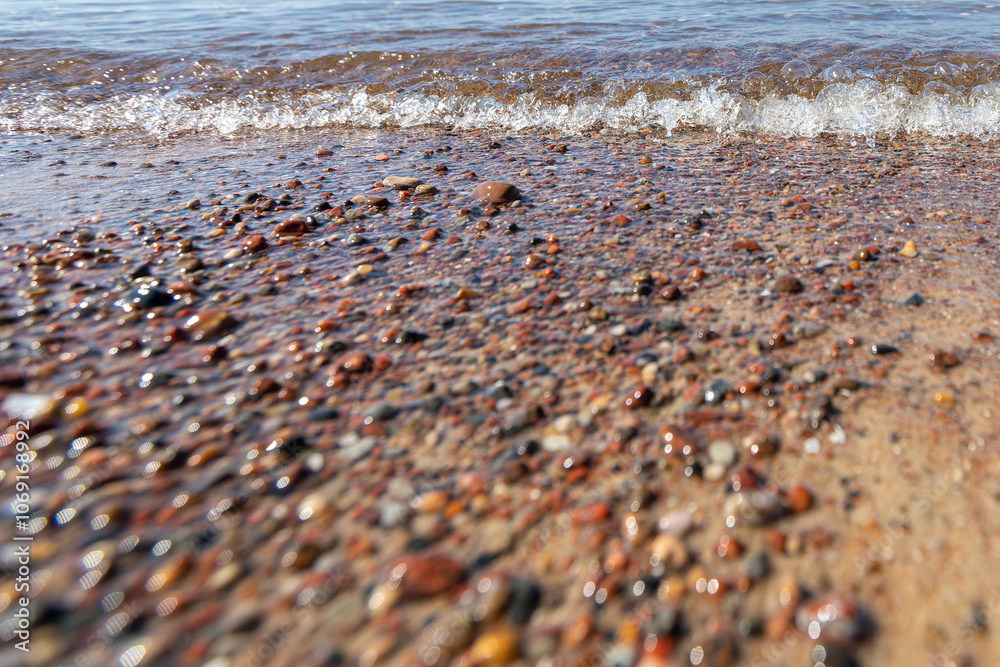 Obraz premium A pebble sea shore with a foaming wave of water. Low angle photo in close-up, low depth of field, nice blur and bokeh