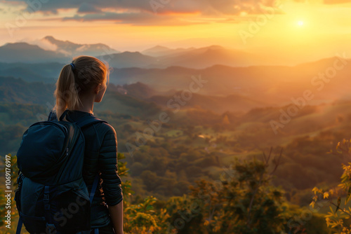 A woman with backpack standing on top of mountain and looking at beautiful view during sunrise.