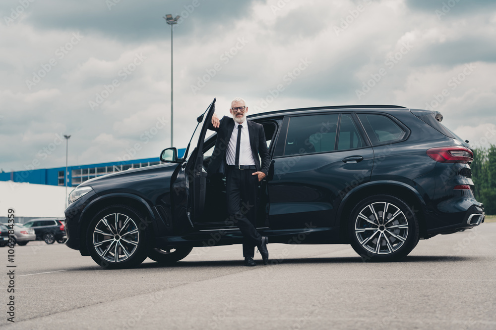 Confident businessman in formal suit stands beside luxury car on city street, embodying success and power