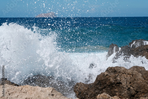 Welle mit viel Gischt bricht an Stein am Strand vor unscharfem Meer und blauem Himmel im Hintergrund bei Kreta photo