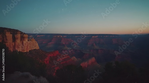 Majestic canyon at sunset with red rock formations glowing warmly in the fading light, and a clear, starry sky overhead. The scene captures the grandeur and tranquility of nature at dusk. photo