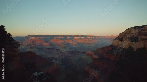 Majestic canyon at sunset with red rock formations glowing warmly in the fading light, and a clear, starry sky overhead. The scene captures the grandeur and tranquility of nature at dusk. photo