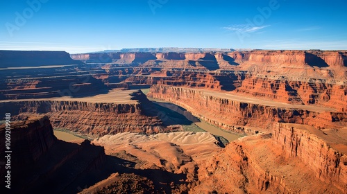 Majestic canyon featuring striking red rock formations, a winding river flowing through its depths, and a bright blue sky overhead