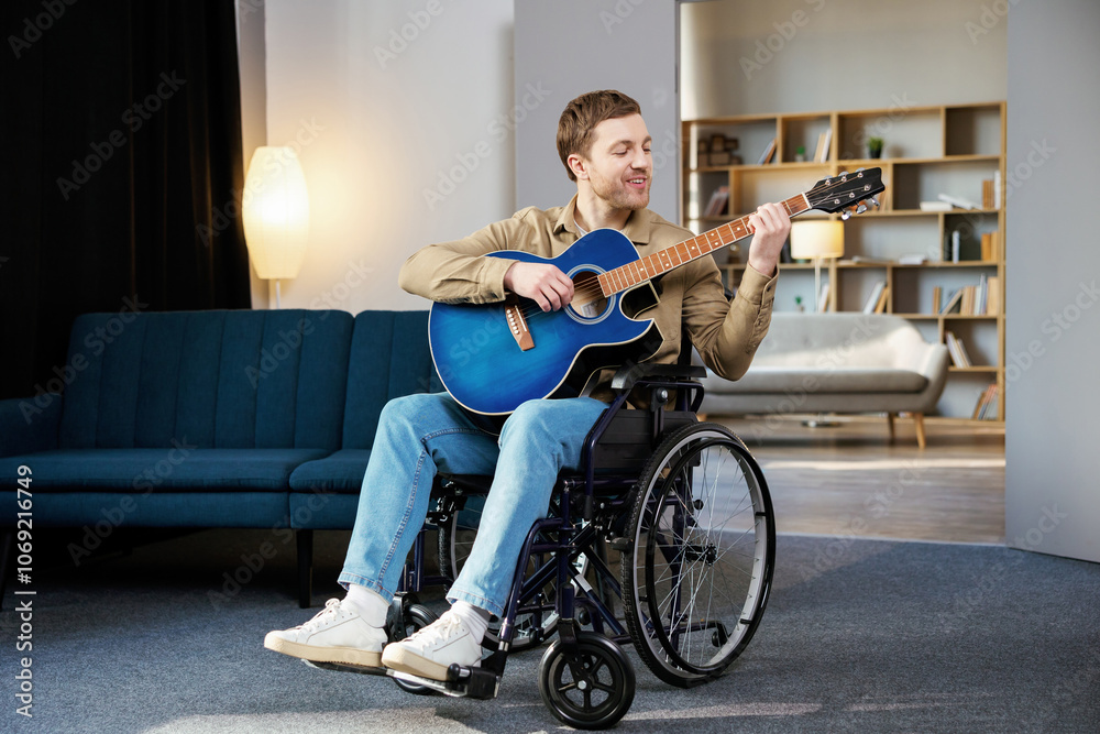 Obraz premium Handsome man with a disability sitting in wheelchair playing on guitar at home