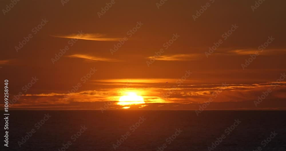 Beautiful golden sunset over the ocean. Sun behind clouds on the horizon with heat haze on a summer evening as birds fly in silhouette.