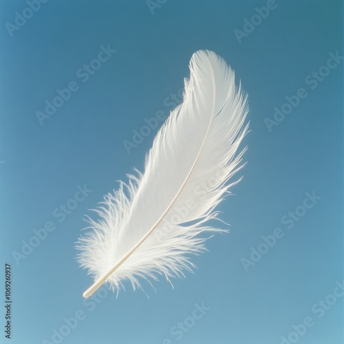 Delicate white feather floating against a clear blue sky