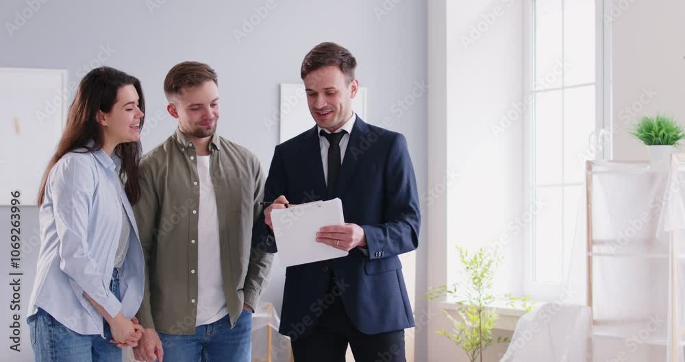 Happy smiling couple talking man with realtor standing in new apartment and going to sign a contract with a real estate agent. Family make a deal and ready to become homeowners. 4k video.