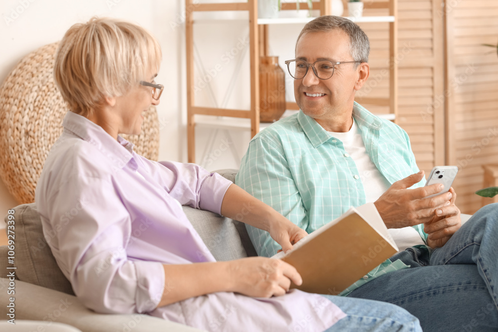 Senior couple with magazine and mobile phone resting in living room Senior couple with magazine and mobile phone resting in living room