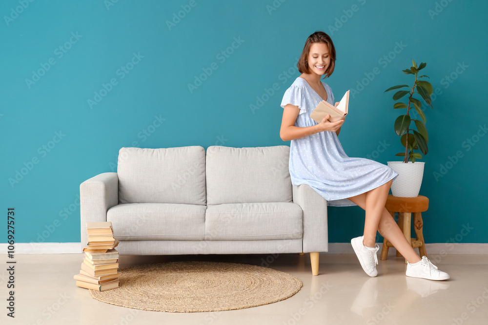 Beautiful young woman reading book near sofa at home Beautiful young woman reading book near sofa at home