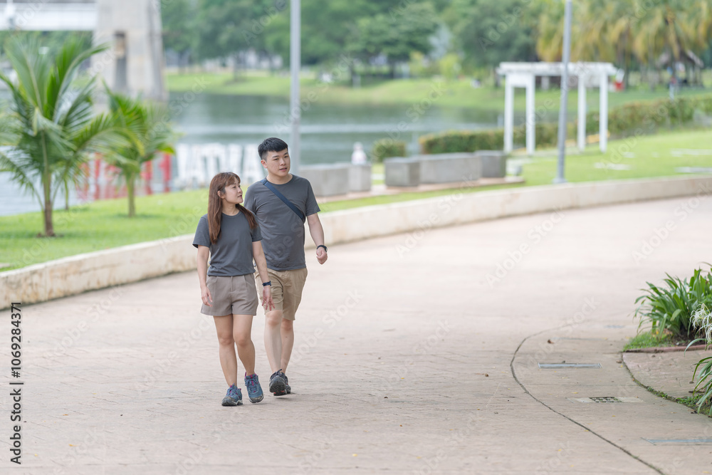 A Chinese-Malaysian couple in their 30s walk together in a green park with abundant water in Kuala Lumpur, Malaysia, on a sunny day in June 2024. A Chinese-Malaysian couple in their 30s walk together in a green park with abundant water in Kuala Lumpur, Malaysia, on a sunny day in June 2024.