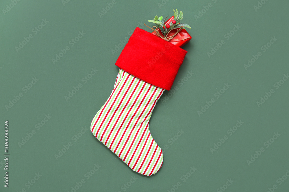 Naklejka premium Christmas sock with gift and mistletoe twig on green background. Top view