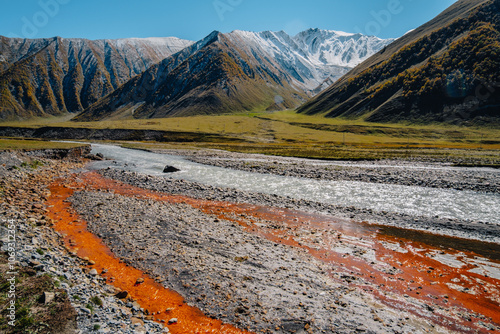 View of the blue and orange (iron-rich) waters of the Terek River, framed by the snowy peaks of the Caucasus in the Truso Gorge near Kazbegi, Georgia