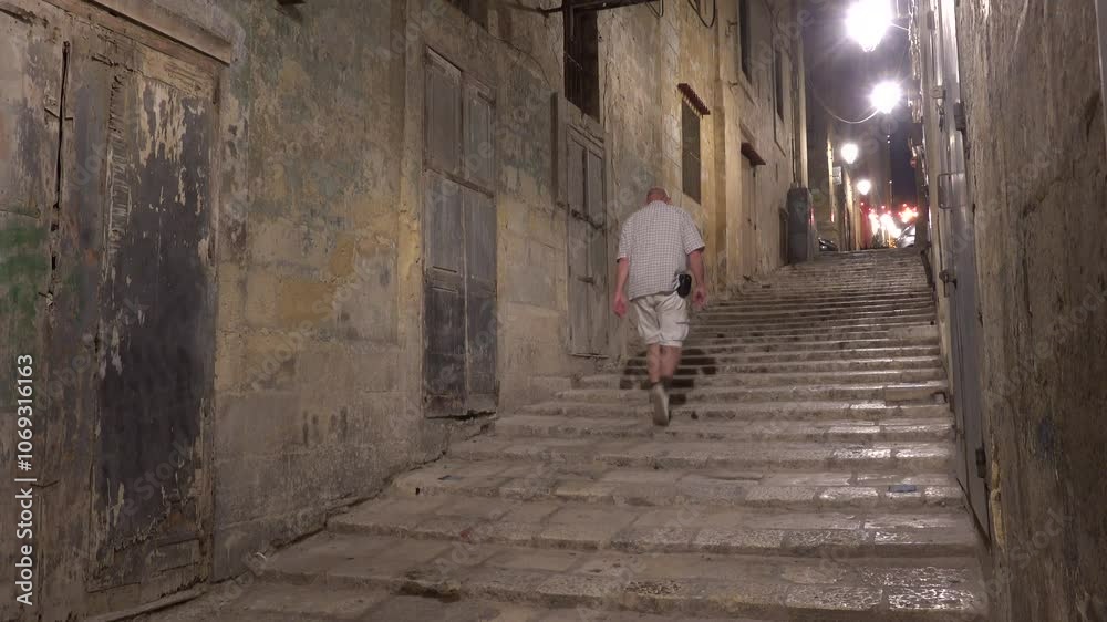 Valletta, Malta A male tourist walks on ancient steps in Old Valletta at night on North Street. Valletta, Malta A male tourist walks on ancient steps in Old Valletta at night on North Street.