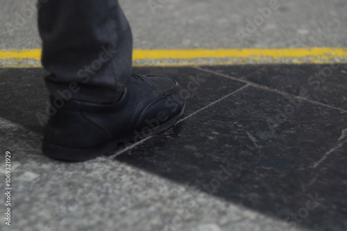 Men's right foot in black soft shoes stands on the marble floor tiles in front of the yellow bounding line. The concept of starting a new path, the first step in a new business photo