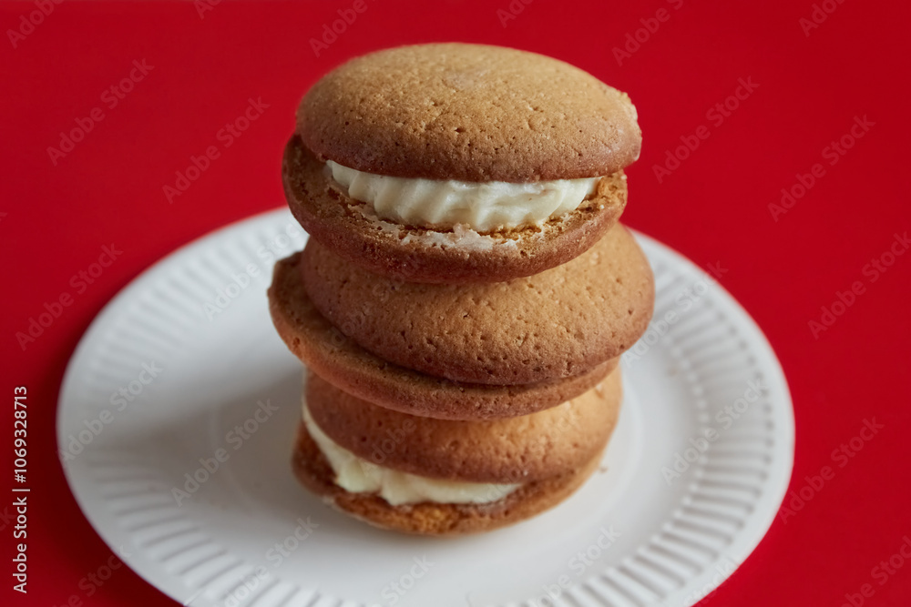 Pumpkin pies stacked on top of each other on a white disposable plate against a red background, pumpkin pies arranged in a tower on a white plate against a red background, traditional desserts. Pumpkin pies stacked on top of each other on a white disposable plate against a red background, pumpkin pies arranged in a tower on a white plate against a red background, traditional desserts.