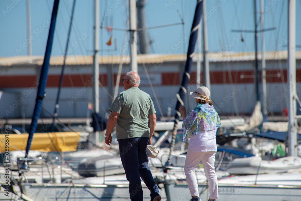 Elderly couple walking along pier surrounded by boats, yachts with masts. Seniors vacation Elderly couple walking along pier surrounded by boats, yachts with masts. Seniors vacation