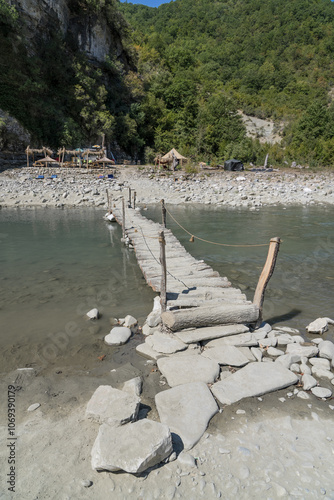 Osumi, Albania - August 15 2024: Handmade rustic wooden bridge (Ura e Vjeter e Zaberzanit) crossing the Osumi River on hot summer day, showcasing traditional Albanian craftsmanship and natural beauty