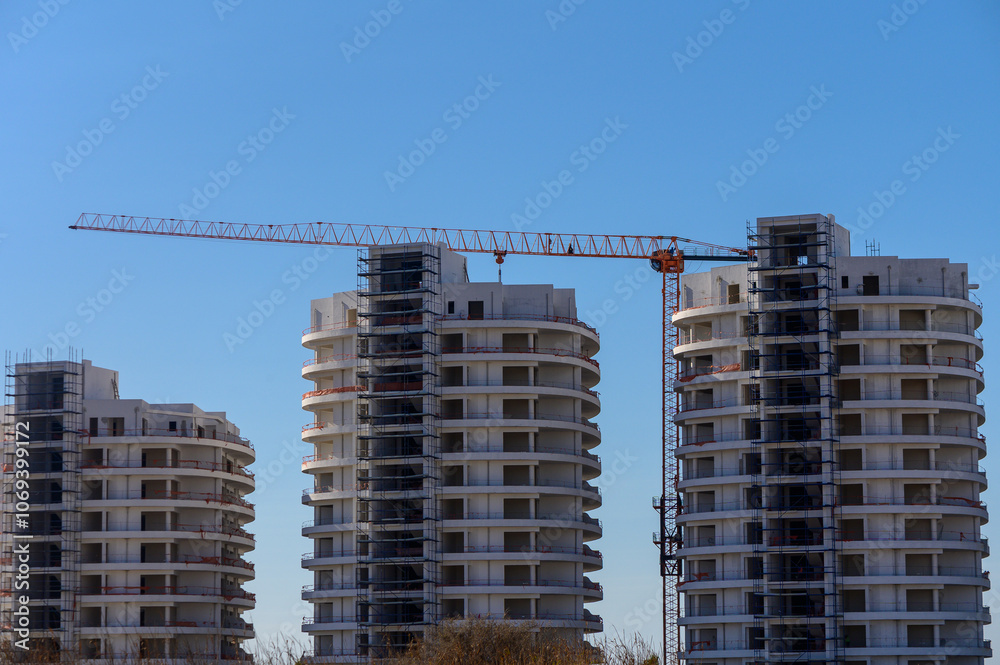 New residential towers under construction with cranes against a clear blue sky in a vibrant urban setting New residential towers under construction with cranes against a clear blue sky in a vibrant urban setting