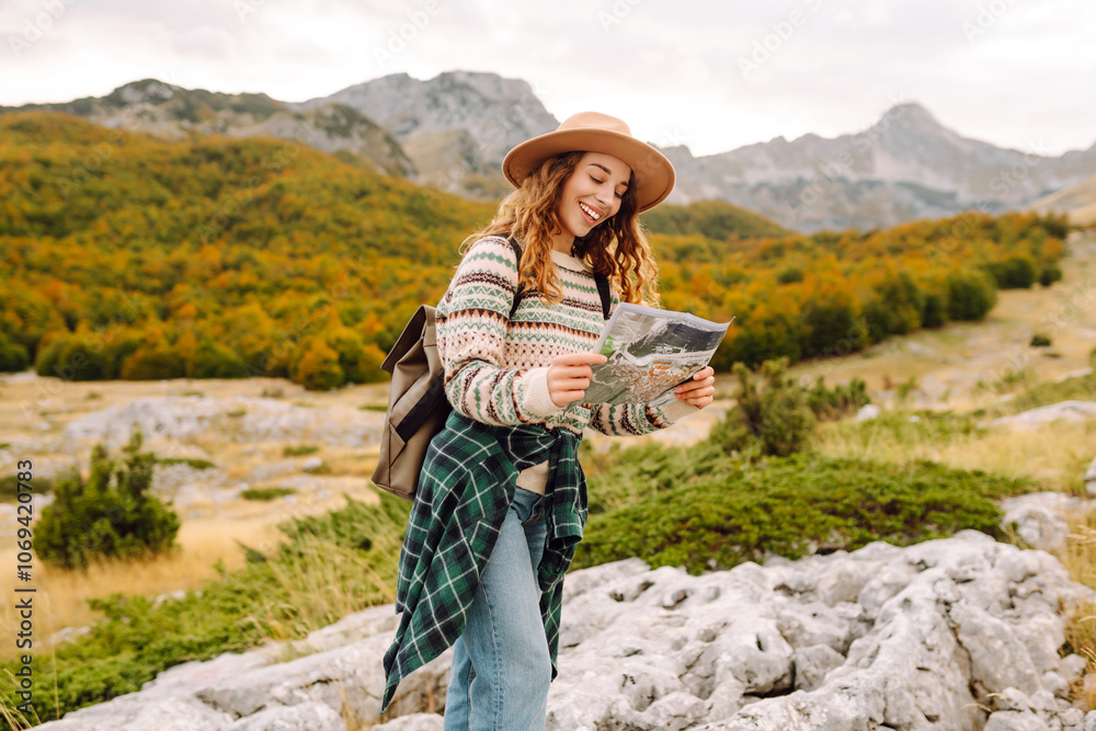 Naklejka premium Female trekker studying a map. Young woman hiking in autumn landscape with a map. Travel, nature concept