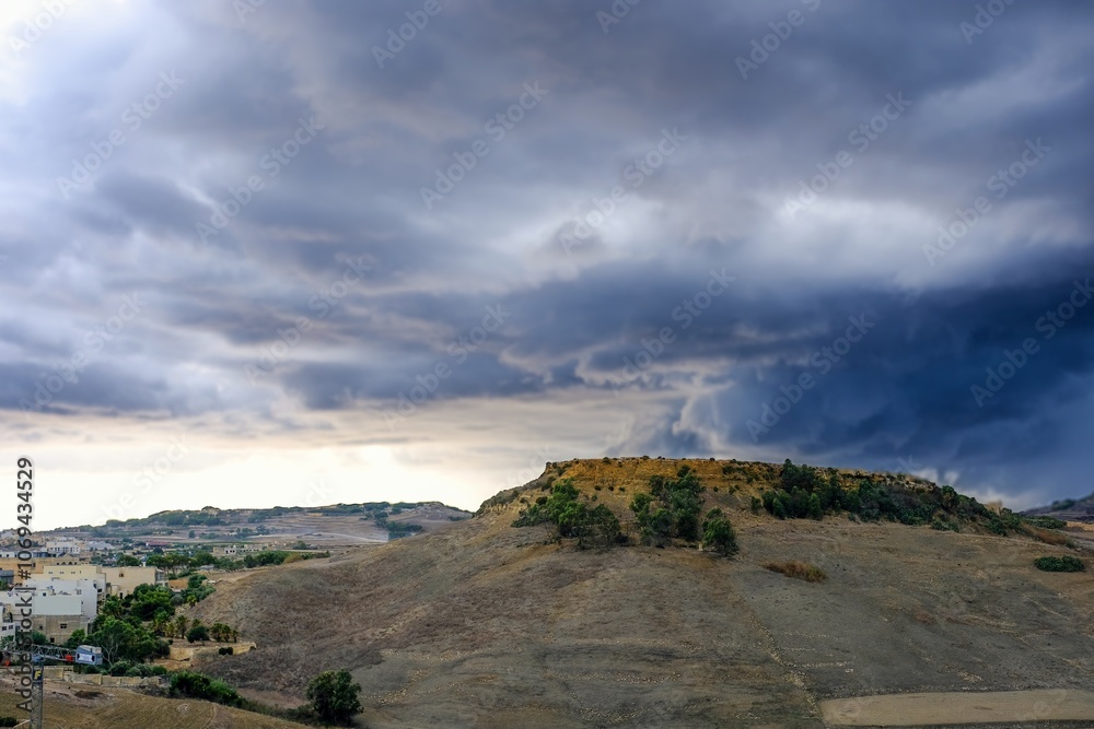 Victoria, Gozo, Malta - a hilltop against a dramatic sky filled with dark clouds. The landscape below includes a mix of greenery and rocky terrain, suggesting a rural or semi-arid environment. Victoria, Gozo, Malta - a hilltop against a dramatic sky filled with dark clouds. The landscape below includes a mix of greenery and rocky terrain, suggesting a rural or semi-arid environment.