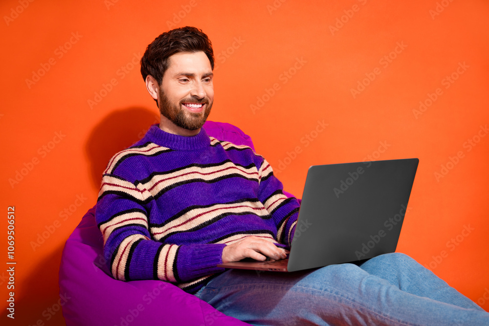 Photo portrait of nice young male sit beanbag wear trendy striped violet outfit isolated on orange color background Photo portrait of nice young male sit beanbag wear trendy striped violet outfit isolated on orange color background