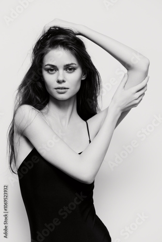 Canvastavla Elegant young woman with long hair posing confidently in a black dress, showcasing beauty and strength against a minimalist white background