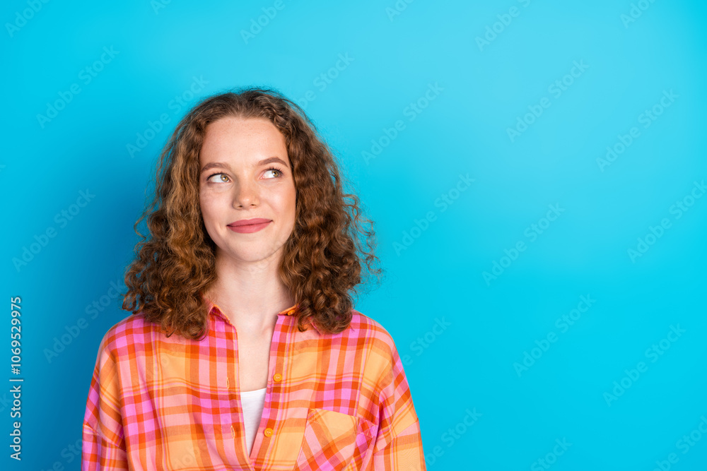 Fototapeta premium Young redhaired woman in casual plaid shirt posing with thoughtful and happy expression against bright blue background