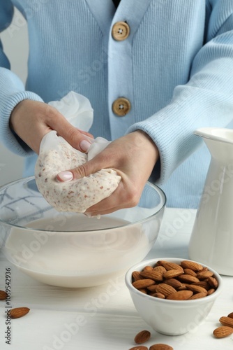 Woman making almond milk at white wooden table, closeup