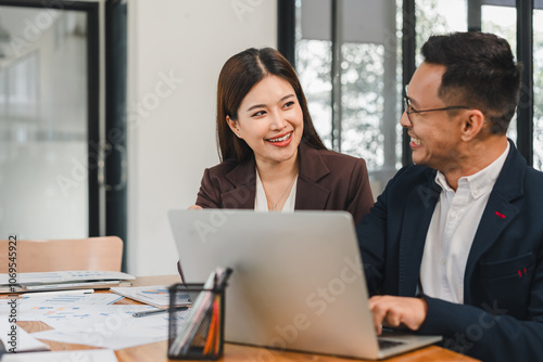 Efficient business meeting with woman and man discussing ideas at laptop. Their smiles reflect collaboration and teamwork in modern office setting