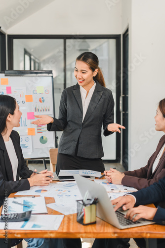 businesswoman presents ideas to colleagues in modern office setting, showcasing charts and graphs. team engages in discussion, highlighting collaboration and professionalism