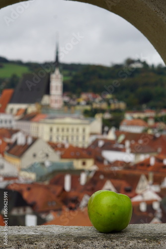 a green apple with the background of Cesky Krumlov view