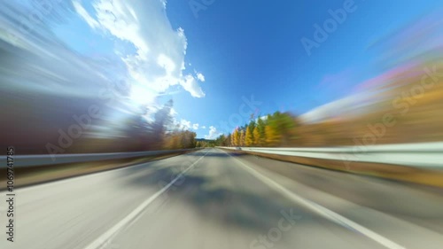 Car Speeding Through a Picturesque Autumn Forest Along a Winding Highway Motion Blur Captures a Car Speeding Along a Highway, Surrounded by Vibrant Autumn Foliage in a Serene Forest Setting photo