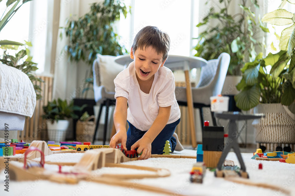 A European child plays with a wooden railway and colored blocks at home. The boy builds a city A European child plays with a wooden railway and colored blocks at home. The boy builds a city