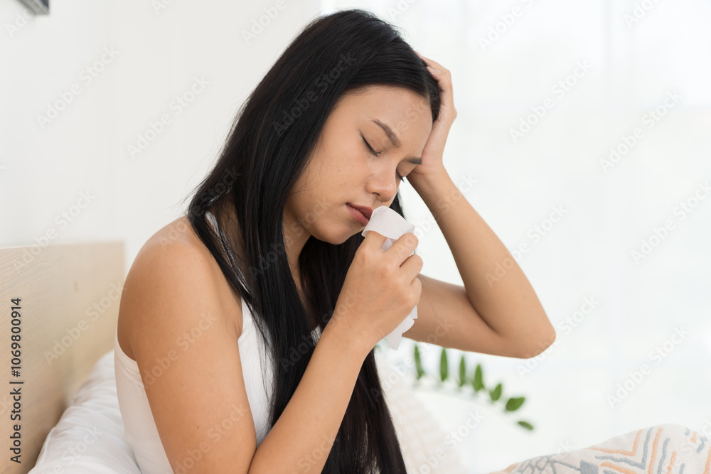 Young Asian woman feeling unwell and have a cough while sitting on the bed. Young woman sick with have a flu. Young woman sick with have a cold Young Asian woman feeling unwell and have a cough while sitting on the bed. Young woman sick with have a flu. Young woman sick with have a cold