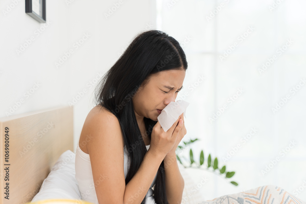 Young Asian woman feeling unwell and have a cough while sitting on the bed. Young woman sick with have a flu. Young woman sick with have a cold Young Asian woman feeling unwell and have a cough while sitting on the bed. Young woman sick with have a flu. Young woman sick with have a cold