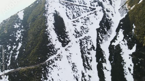 Drone ascends, unveiling snowy mountain trail to Veliki Raskovec in Slovenia photo