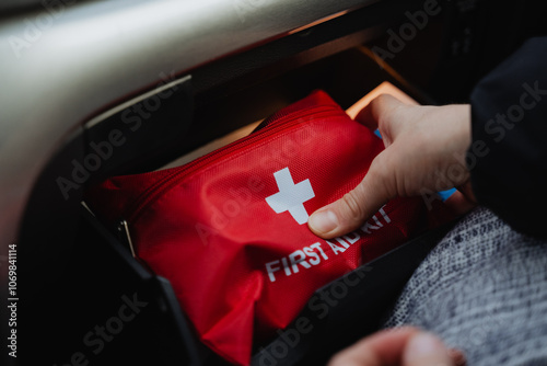 A person is carefully placing a first aid kit into the trunk of a car, ensuring it is securely stored for easy access in case of an emergency or medical situation arising during travel photo