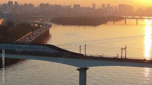 A subway train crossing Dangsan Bridge in Seoul against a backdrop of a reddish-yellow sunrise