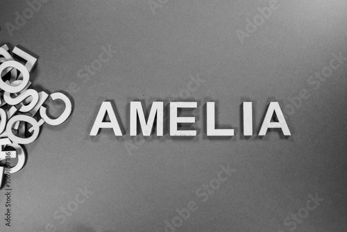 Popular and modern baby girl fashion name AMELIA in wooden English language capital letters spilling from a pile of letters on a red background in black and white