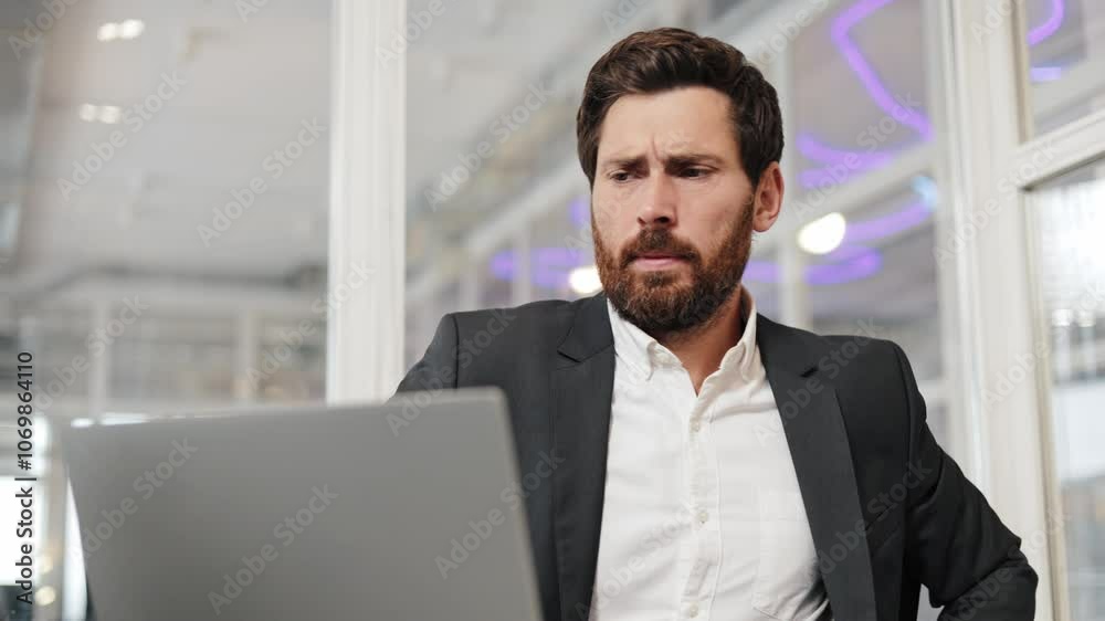 Businessman stretches his arms at his desk in an office while looking at a laptop. He is wearing a suit and is at work. Businessman stretches his arms at his desk in an office while looking at a laptop. He is wearing a suit and is at work.